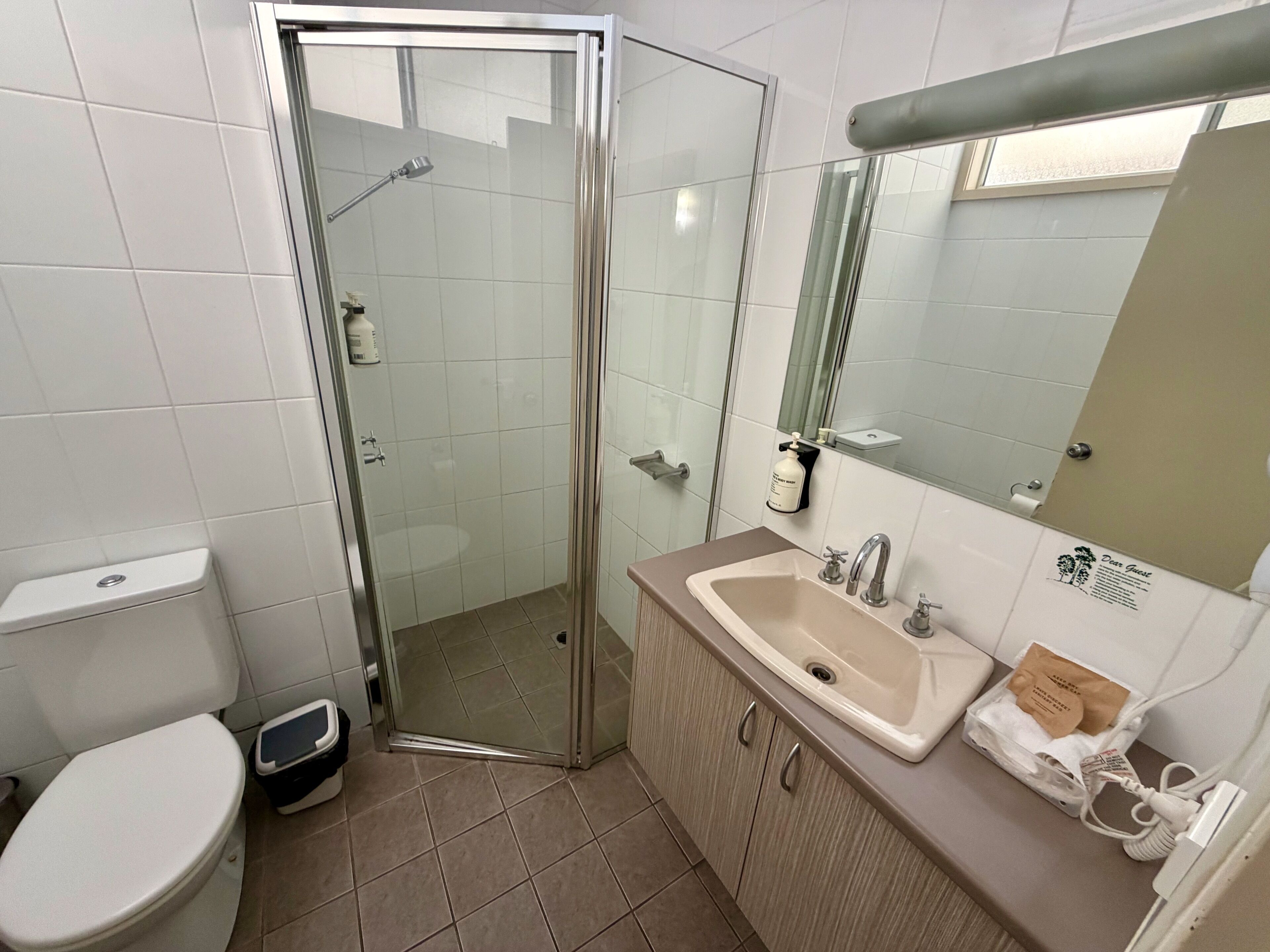Un baño con ducha de vidrio, lavamanos con espejo y retrete.