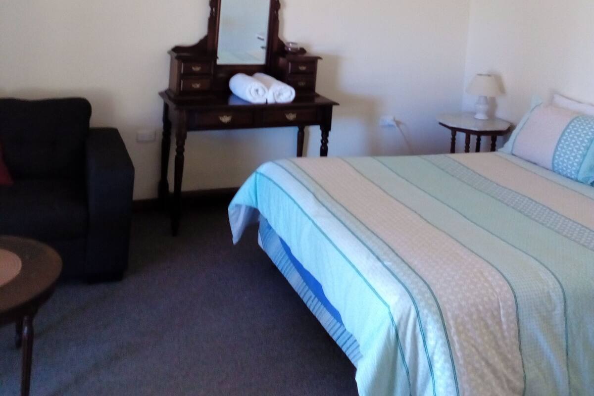 Een slaapkamer met een bed, een dressoir met spiegel, een stoel en een klein tafeltje.