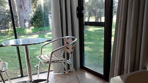 Quarto com porta de vidro que dá para um jardim, uma cadeira de estrutura metálica e uma mesa redonda pequena.