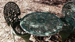 Um jardim com mesa e cadeiras, rodeado por um muro de pedra e uma árvore.