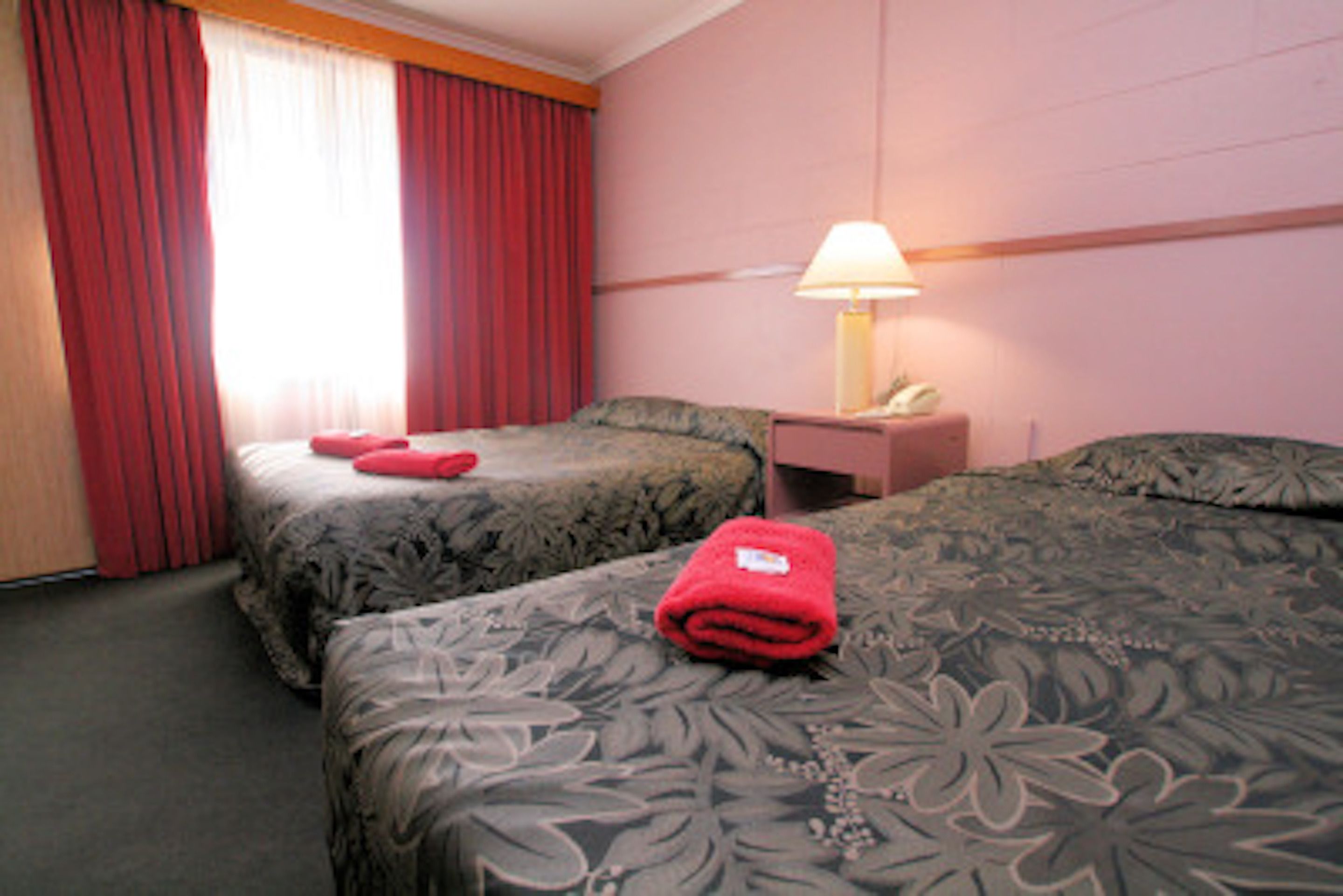 Une chambre d’hôtel avec deux lits, une table de chevet avec une lampe et des rideaux rouges.