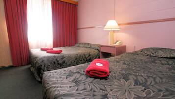 Une chambre d’hôtel avec deux lits, une table de chevet avec une lampe et des rideaux rouges.