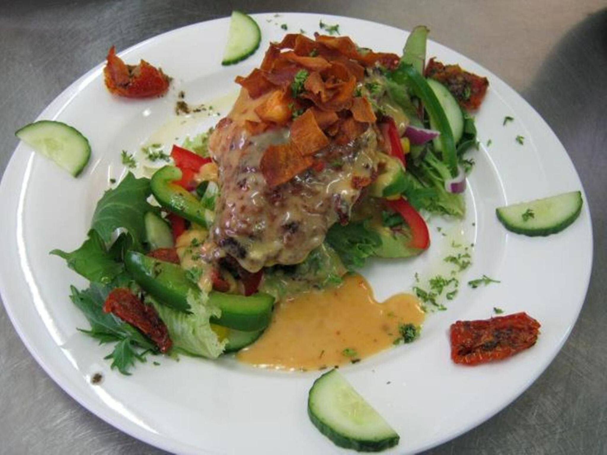 A plate with a grilled chicken breast, mixed vegetables, and a side of sauce.