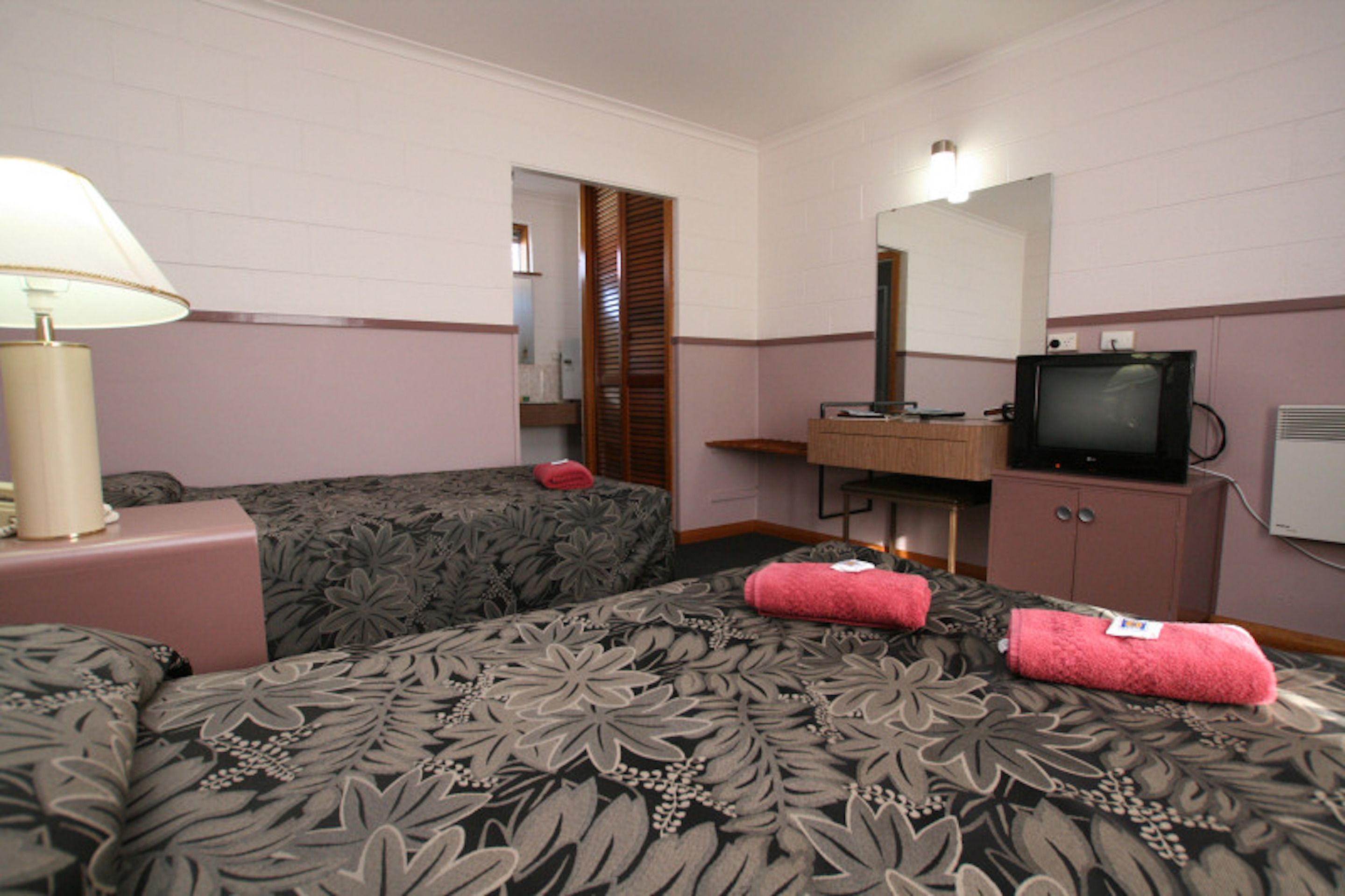 Habitación de hotel con dos camas, televisión, espejo y mesita de noche con lámpara.