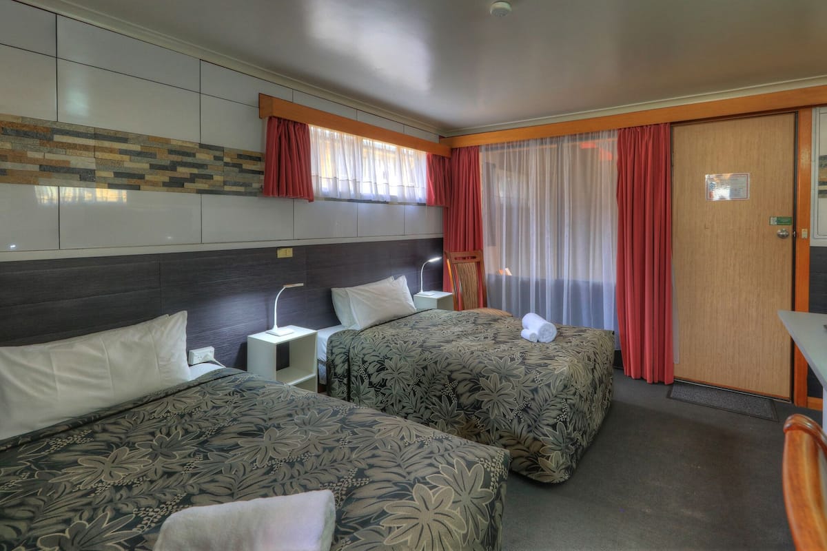 Ein Hotelzimmer mit zwei Betten, einem Schreibtisch, einem Fernseher und einer Badezimmertür.