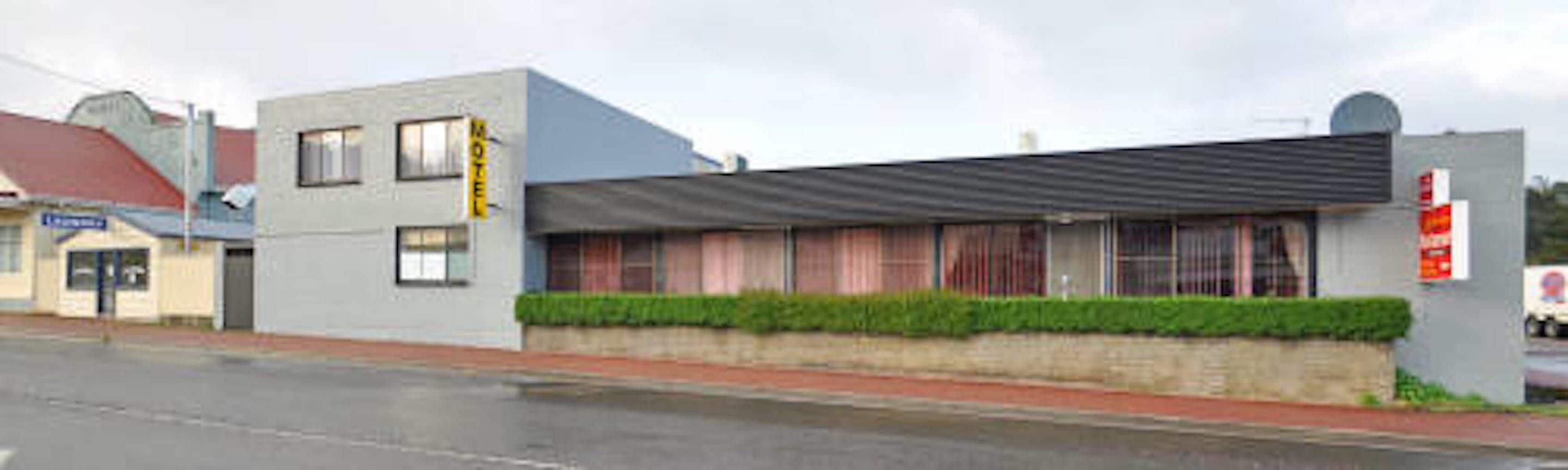 A motel with a flat roof, a small front garden, and a visible signboard.