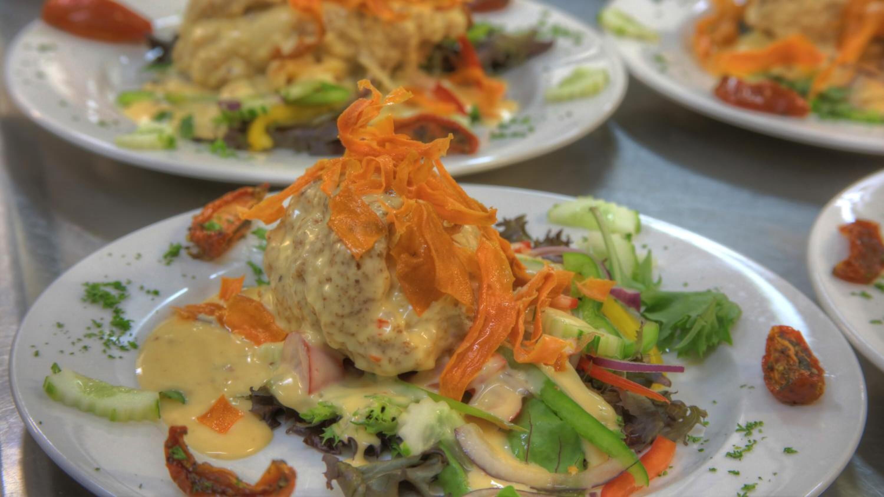 A variety of plated dishes with a focus on a central dish topped with shredded carrots and a creamy sauce.