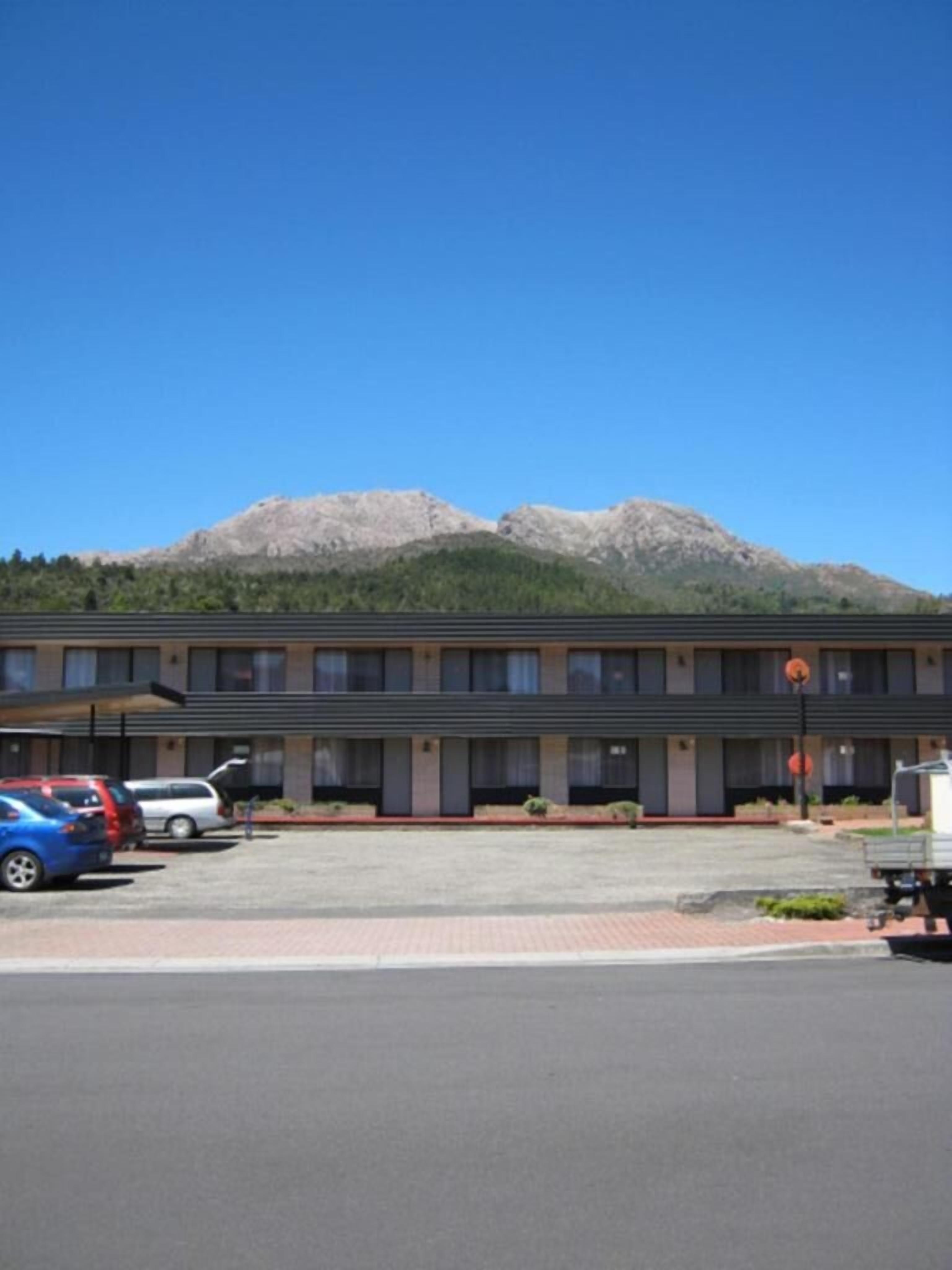 Een motel met een parkeerplaats, een berg op de achtergrond en een heldere lucht.