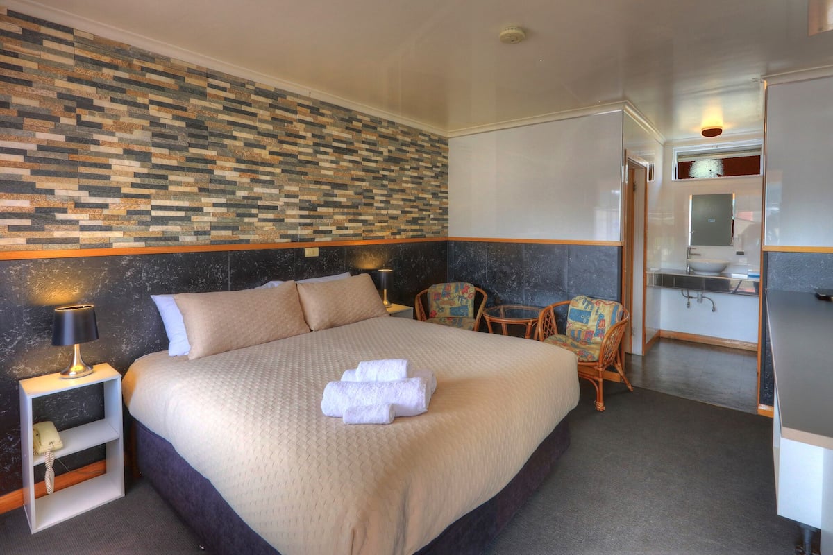 Ein Hotelzimmer mit einem großen Bett, einem kleinen Tisch, zwei Stühlen, einem Schreibtisch mit Spiegel und einem Fernseher.
