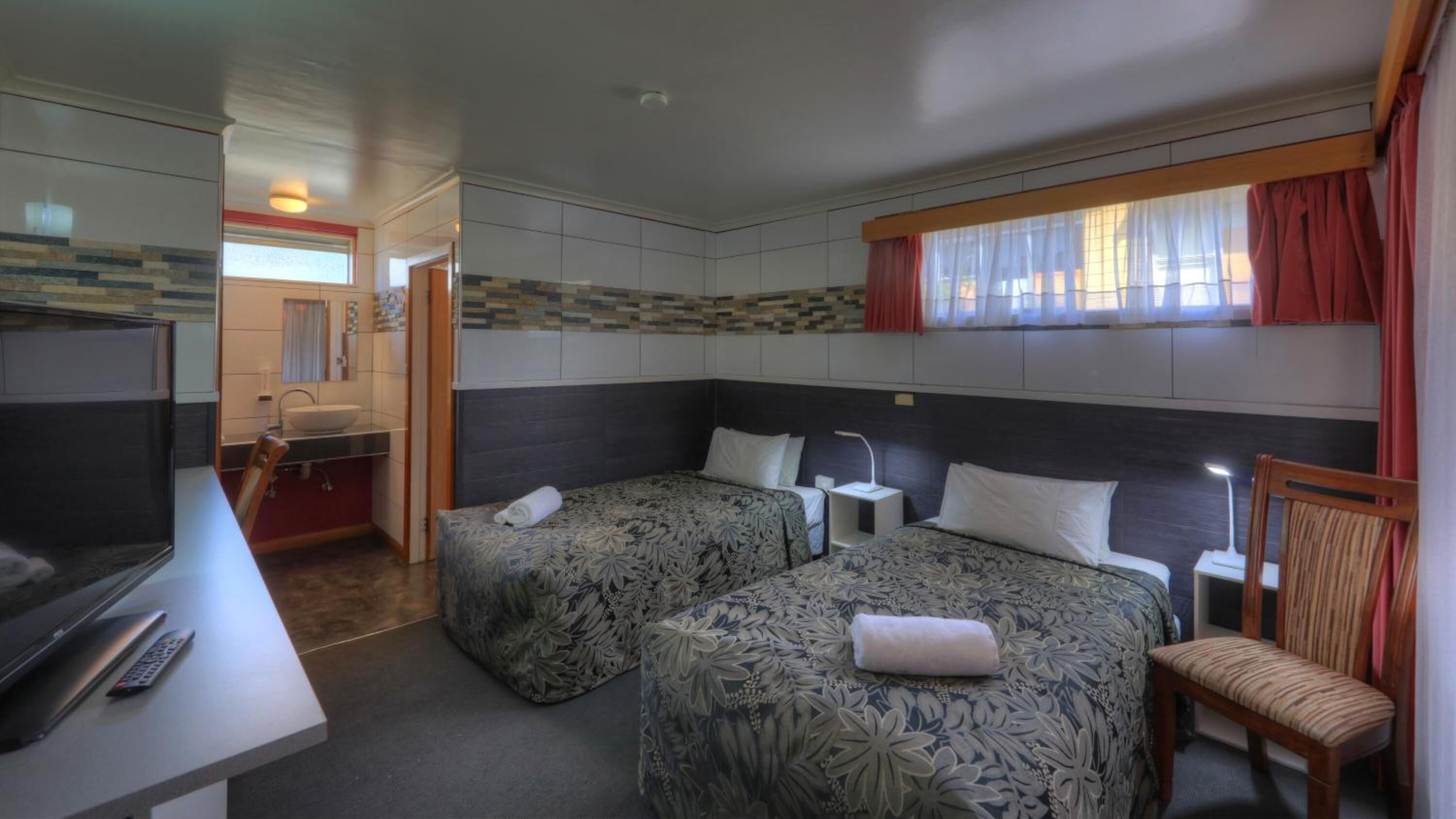 Habitación de hotel con dos camas, televisión, escritorio y baño.