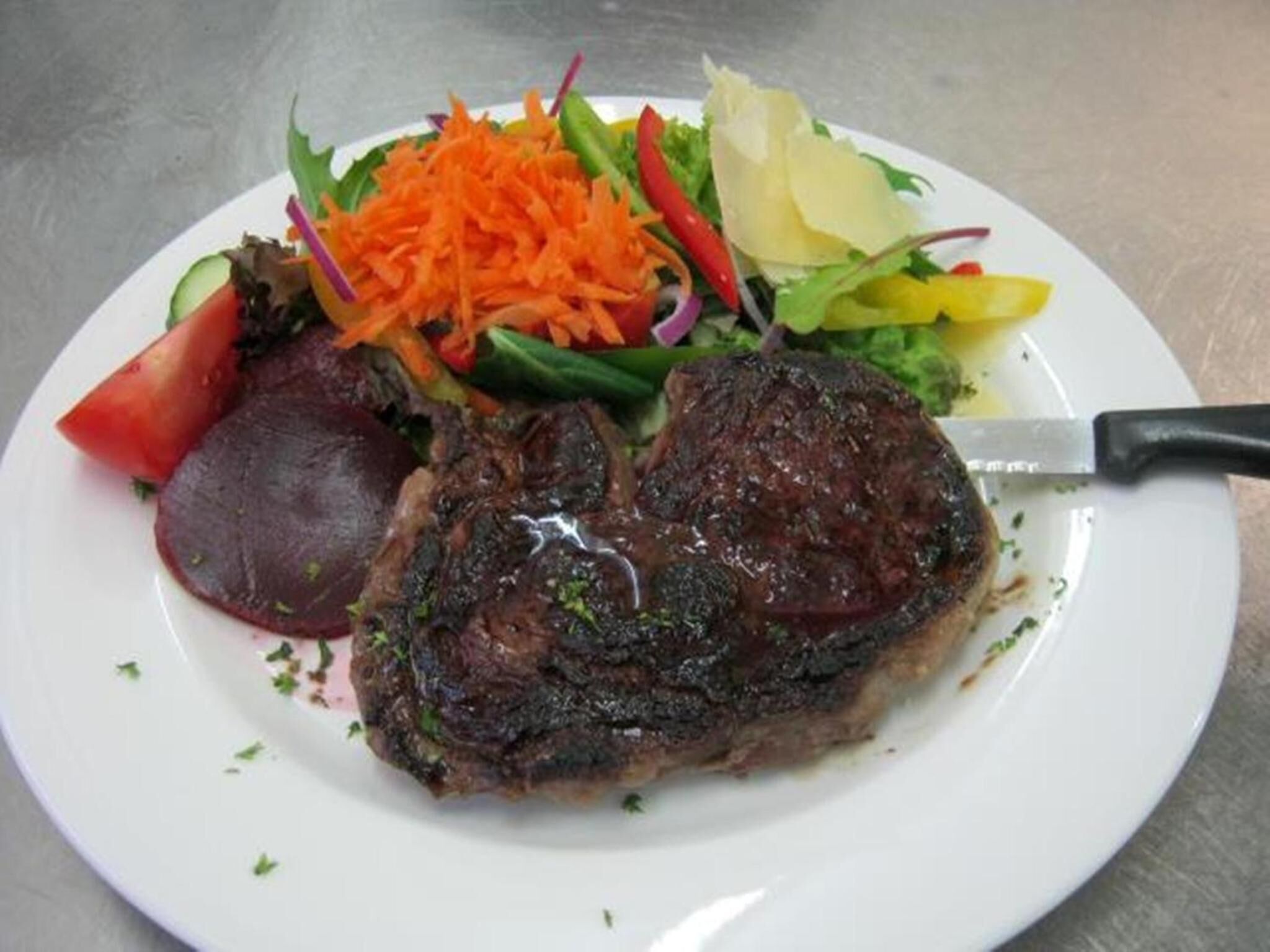 A plate with a steak, vegetables, and a knife.