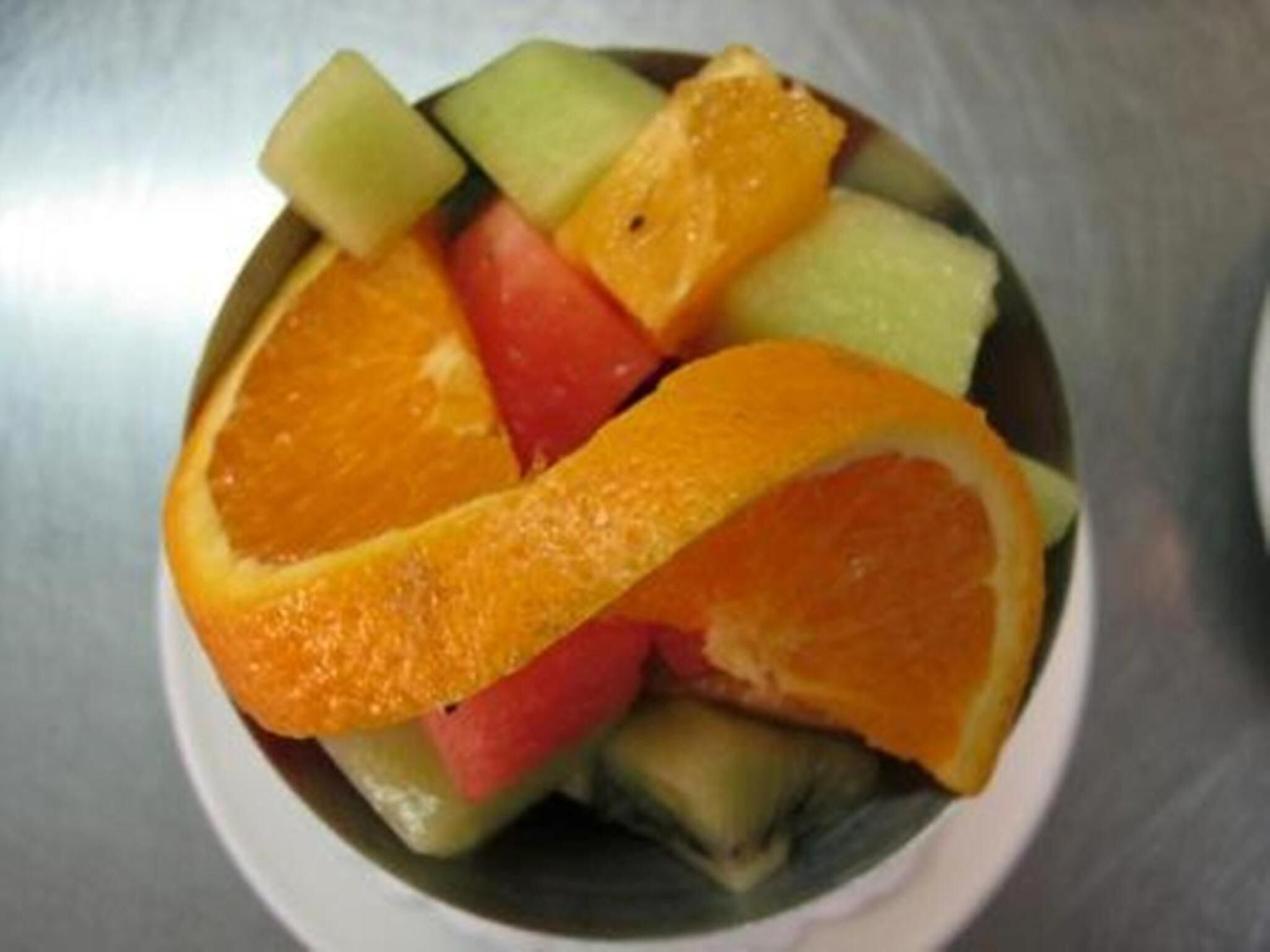 Un cuenco con fruta, incluyendo naranjas, manzanas y melón.