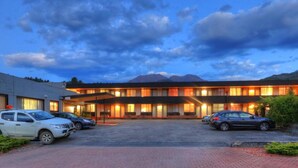 Hotel amb un pàrquing, edifici amb diverses finestres, i una muntanya al fons.