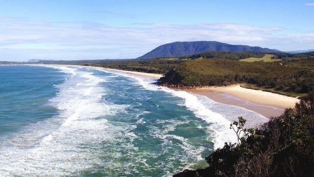 A coastal landscape with a beach, ocean waves, and a mountain in the background. - Seaview Bed and Breakfast (Bonny Hills)