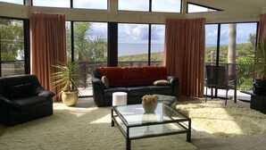 A spacious living room with a large glass coffee table, a black sofa with a red throw blanket, and a view of the ocean through large windows. - Seaview Bed and Breakfast (Bonny Hills)