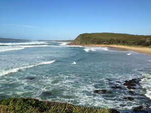 A coastal landscape with waves crashing onto a sandy beach, surrounded by greenery. - Seaview Bed and Breakfast (Bonny Hills)