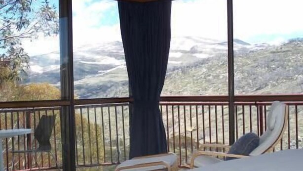 Una habitació amb un llit, una cadira i una taula. Hi ha una finestra gran que ofereix vistes a un paisatge de muntanya.