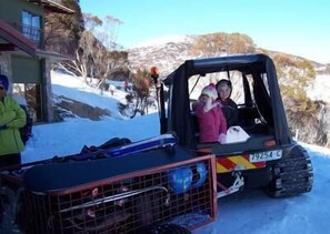 A snowmobile with a license plate, a person in a pink jacket, and another in a green jacket standing beside it. - Guthega Inn (Wilsons Valley)