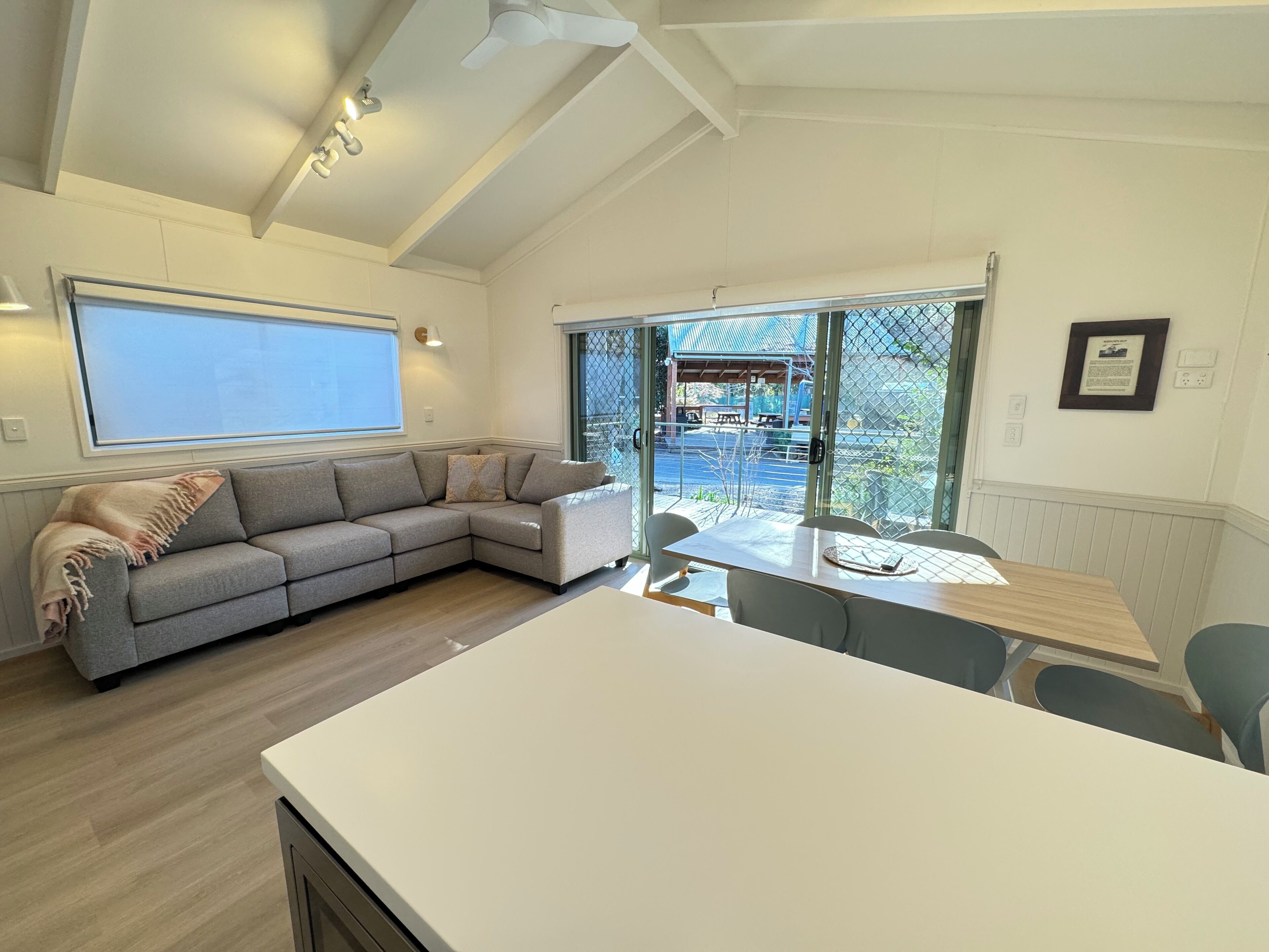 Een moderne woonkamer met een hoekbank, een eettafel met stoelen en een groot raam met uitzicht op een terras.
