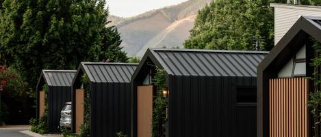 Una hilera de cabañas modernas con techos negros y detalles de madera, frente a un telón de fondo de vegetación exuberante y montañas.
