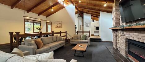 A cozy living room with a high wooden ceiling, a fireplace, and a comfortable seating area.