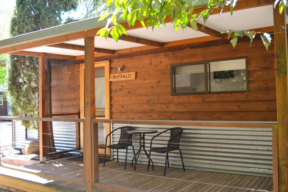 A wooden cabin with a covered porch, two chairs, and a table.
