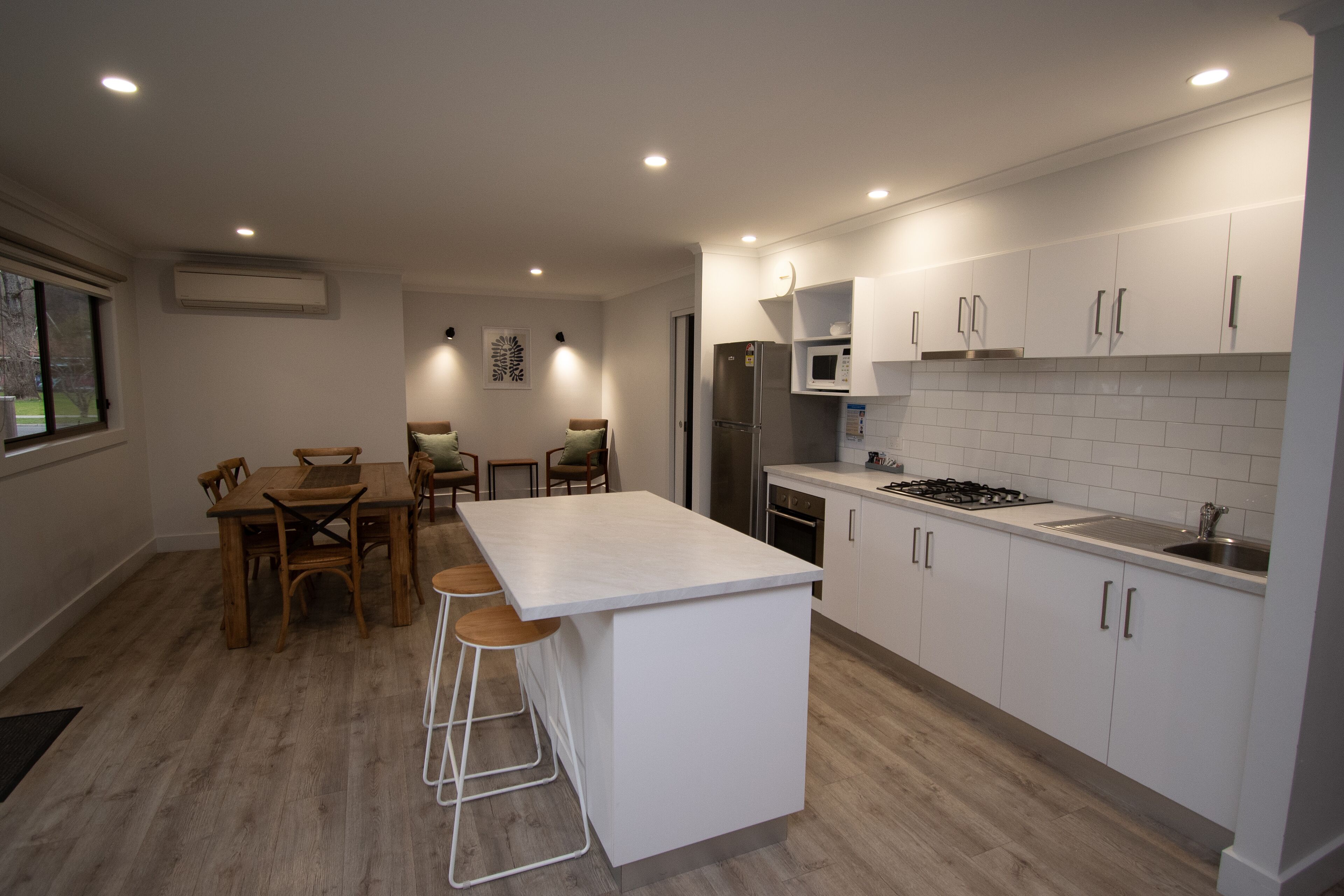 A modern kitchen with white cabinets, a central island with stools, a refrigerator, microwave, and a gas stove.