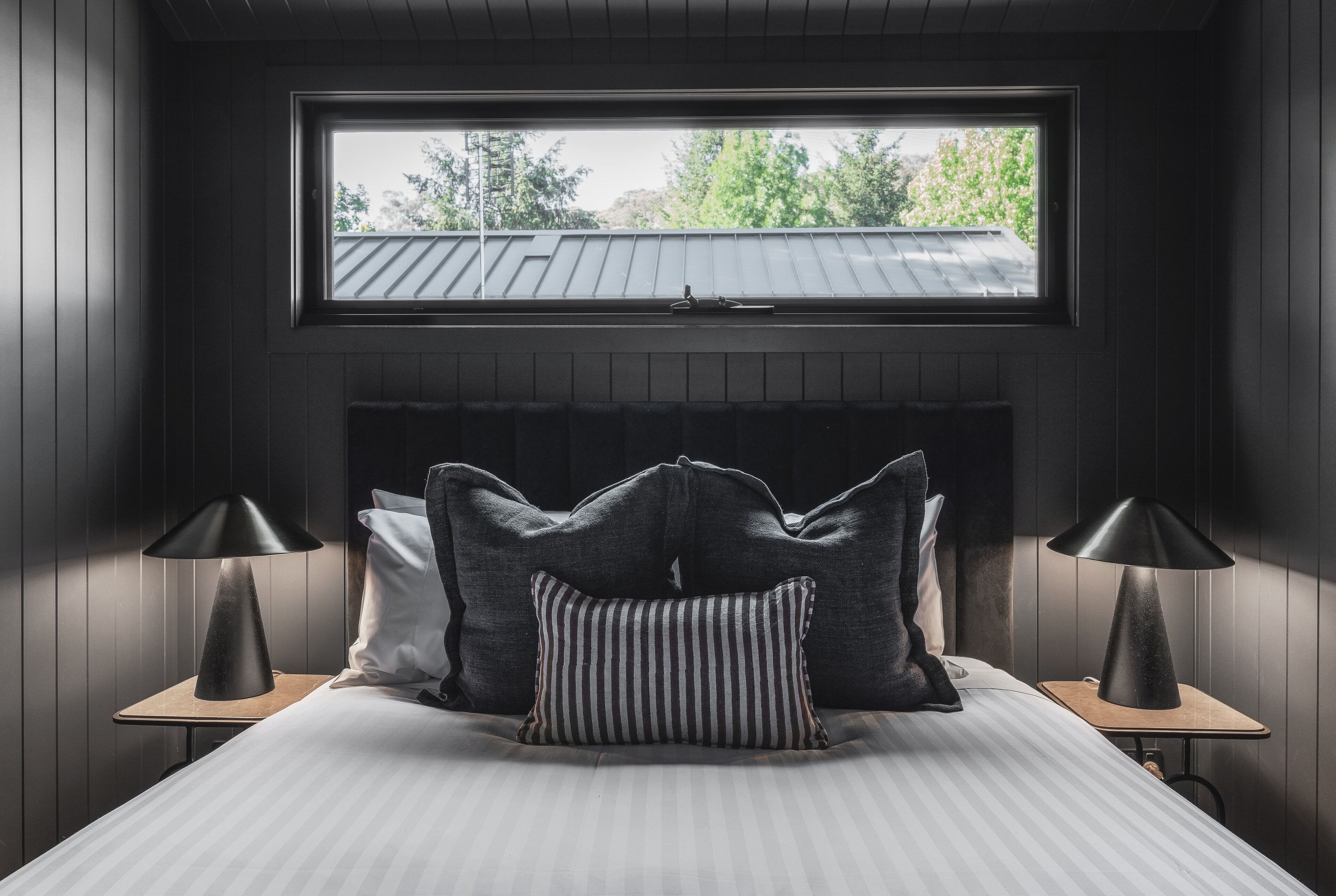 A bedroom with a bed, two bedside tables, a window, and a radiator.