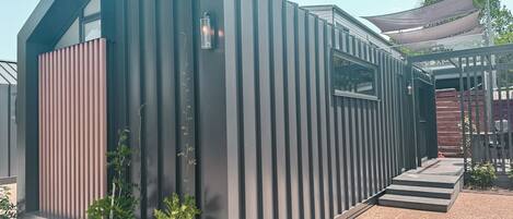 Een modern, gelijkvloers gebouw met een schuin dak, een verticale houten gevelbekleding aan de linkerkant en een klein raam.