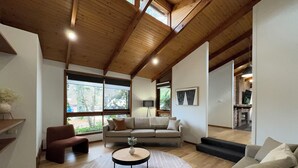 A spacious living room with a high ceiling, wooden beams, a large window, a sofa, a coffee table, and a fireplace. - Big4 Tasman Holiday Parks - Bright (Bright)