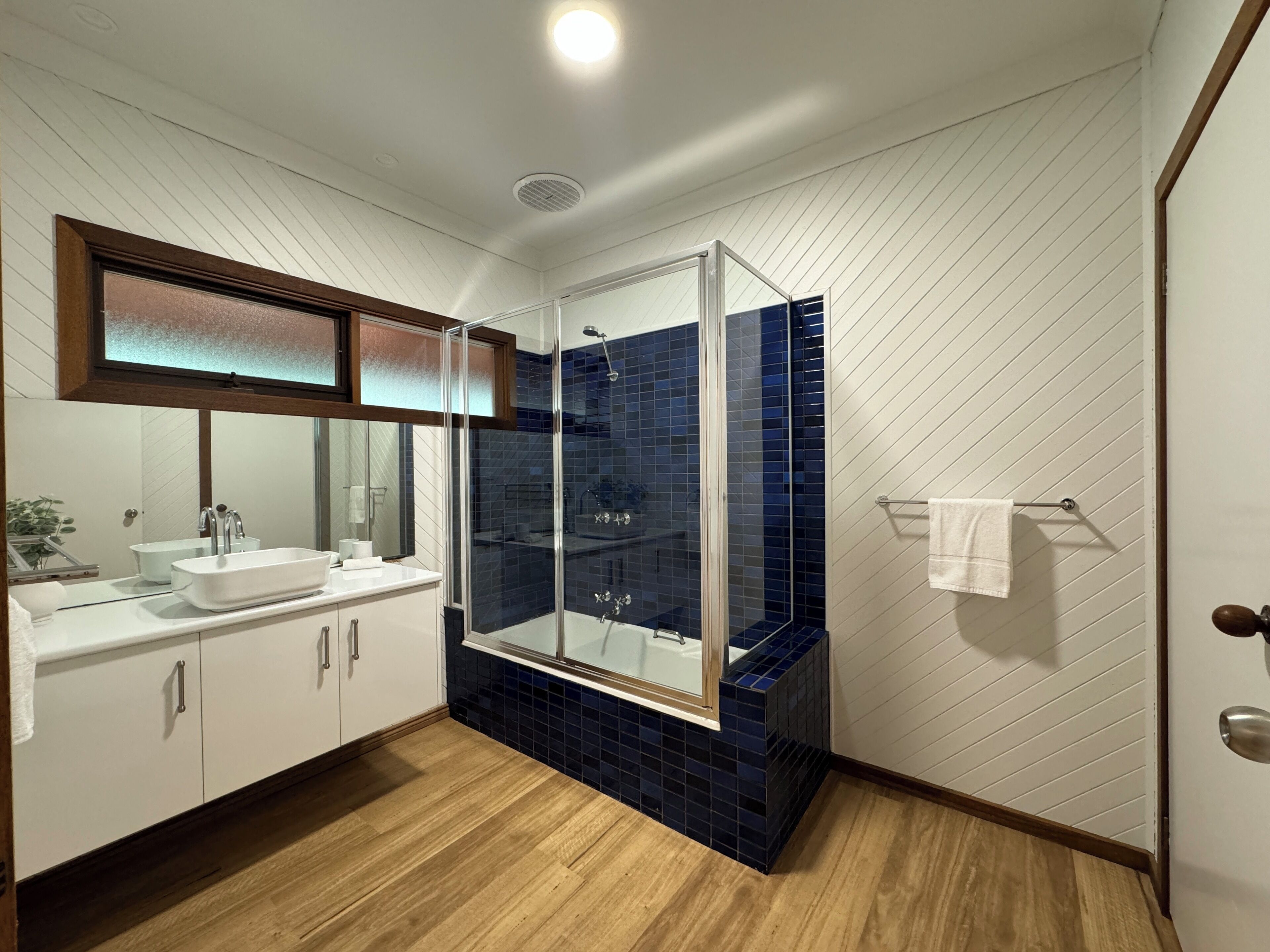 A modern bathroom with a glass-enclosed shower, white cabinets, and a wooden floor.