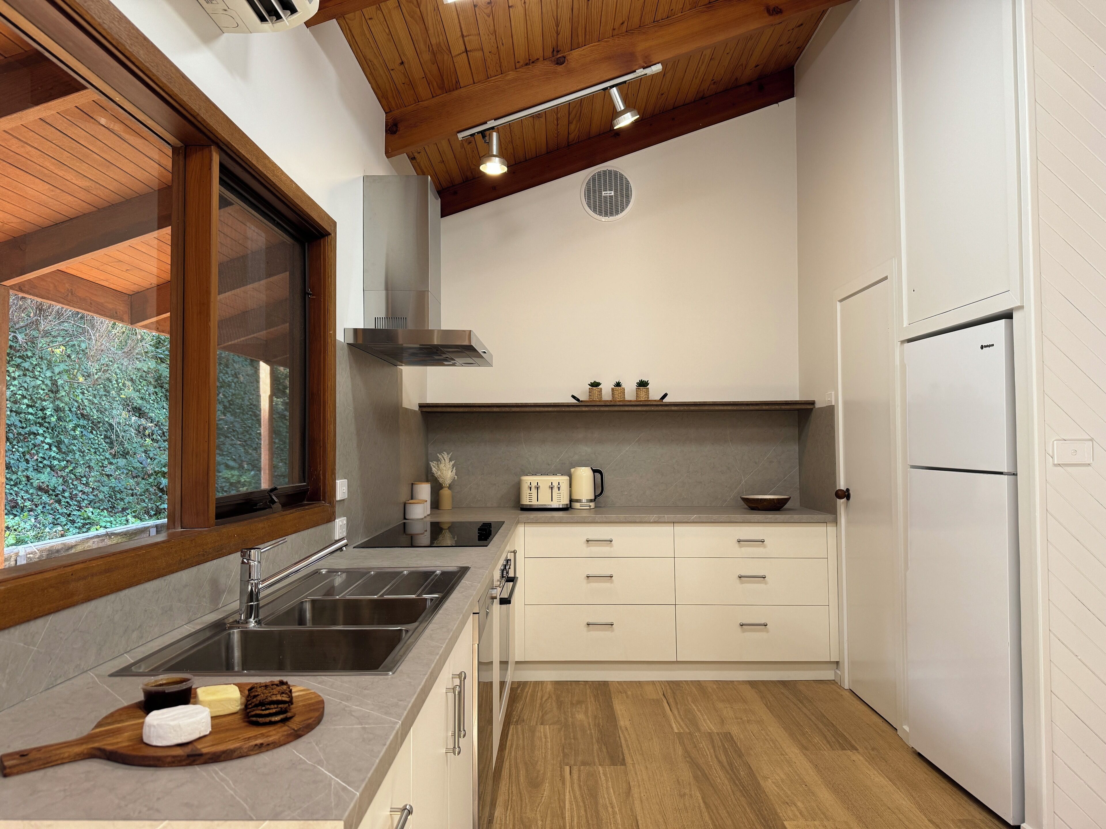 A modern kitchen with a wooden ceiling, a built-in stove, a sink, and a refrigerator.