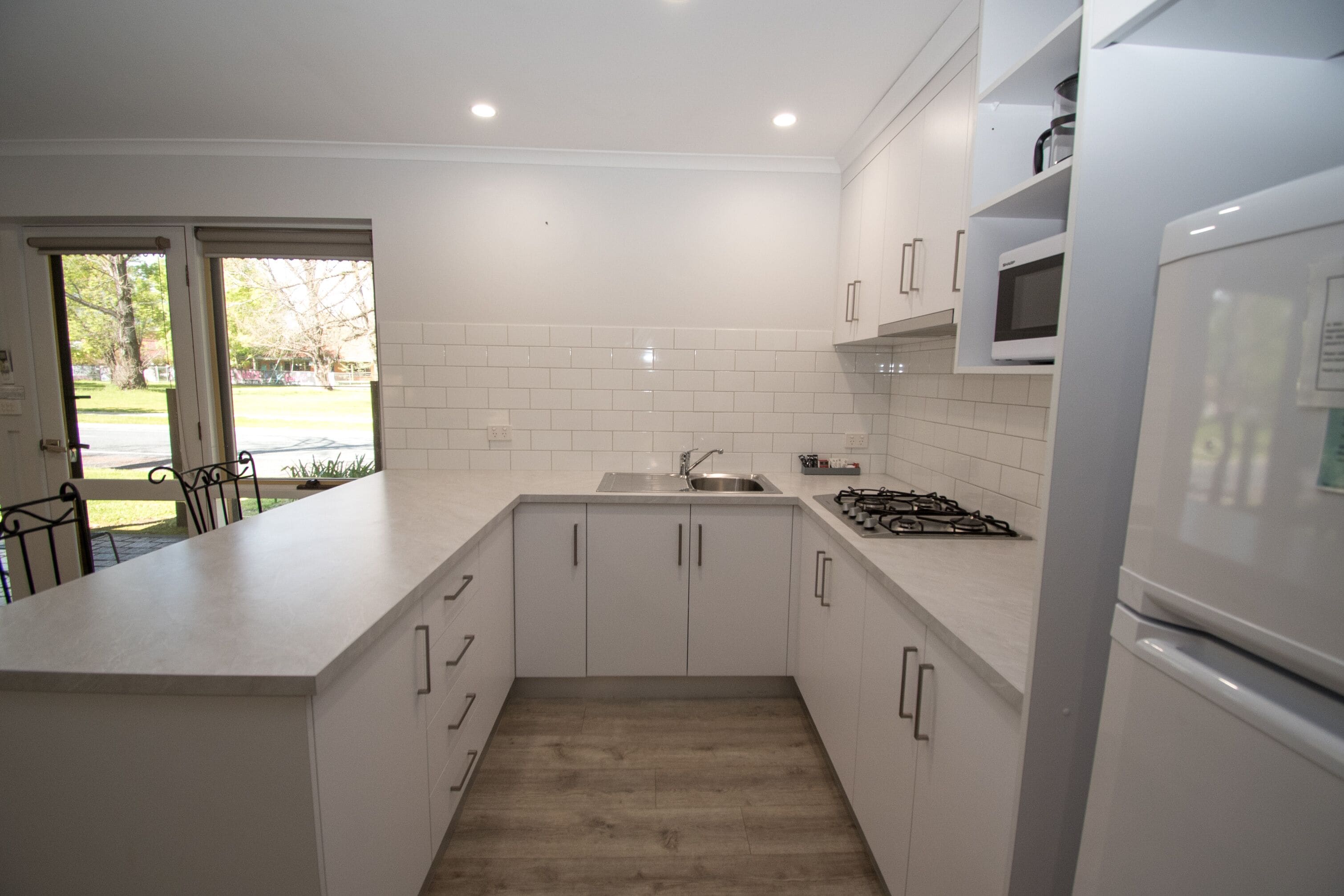 A modern kitchen with white cabinets, a stainless steel sink, a microwave, and a refrigerator.