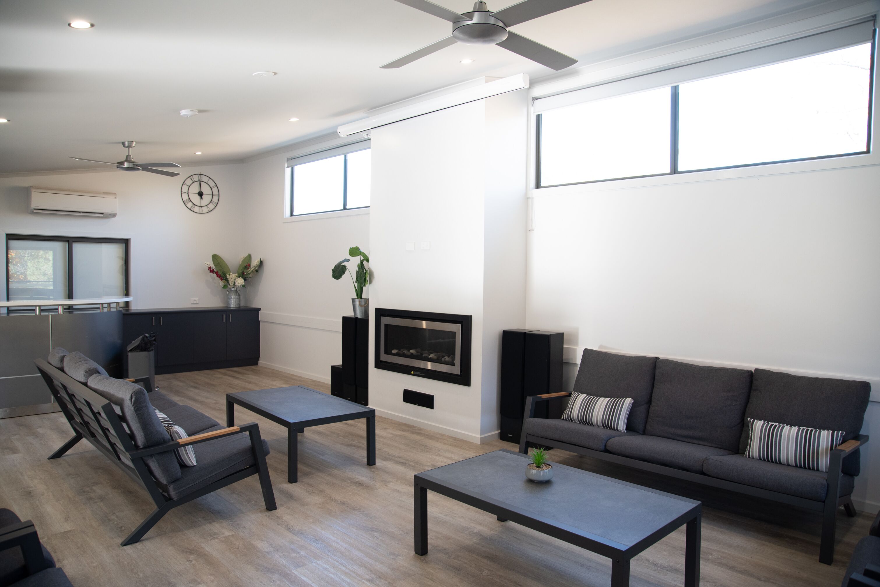 A modern living room with a sofa, coffee table, and TV. There is a kitchen area with cabinets and a window.