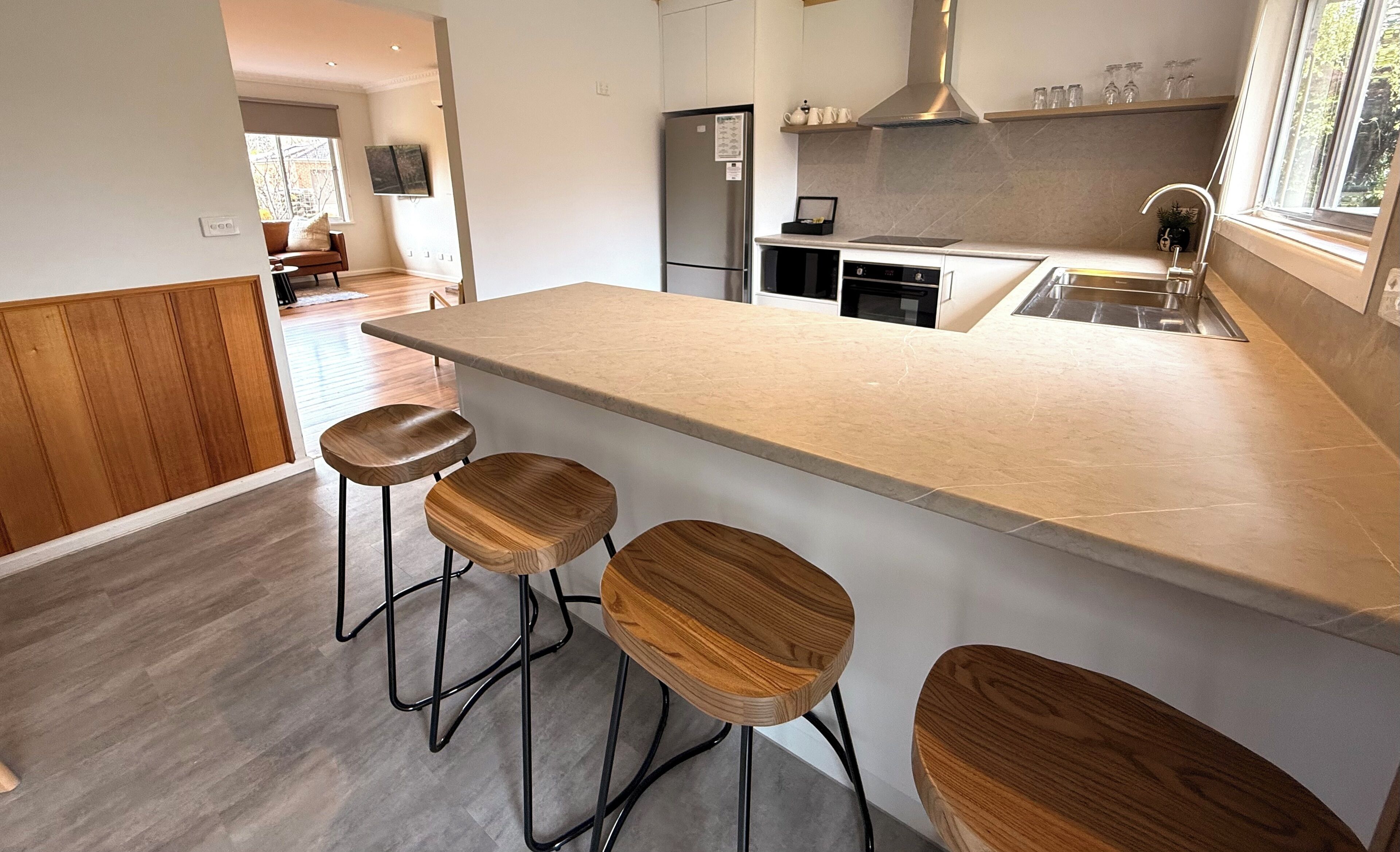 Una cocina moderna con una isla central, taburetes de bar, un refrigerador y una ventana con vistas.