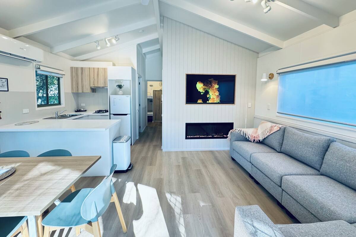 A modern kitchen with a central island, a dining area with a table and chairs, a grey sofa, and a fireplace.