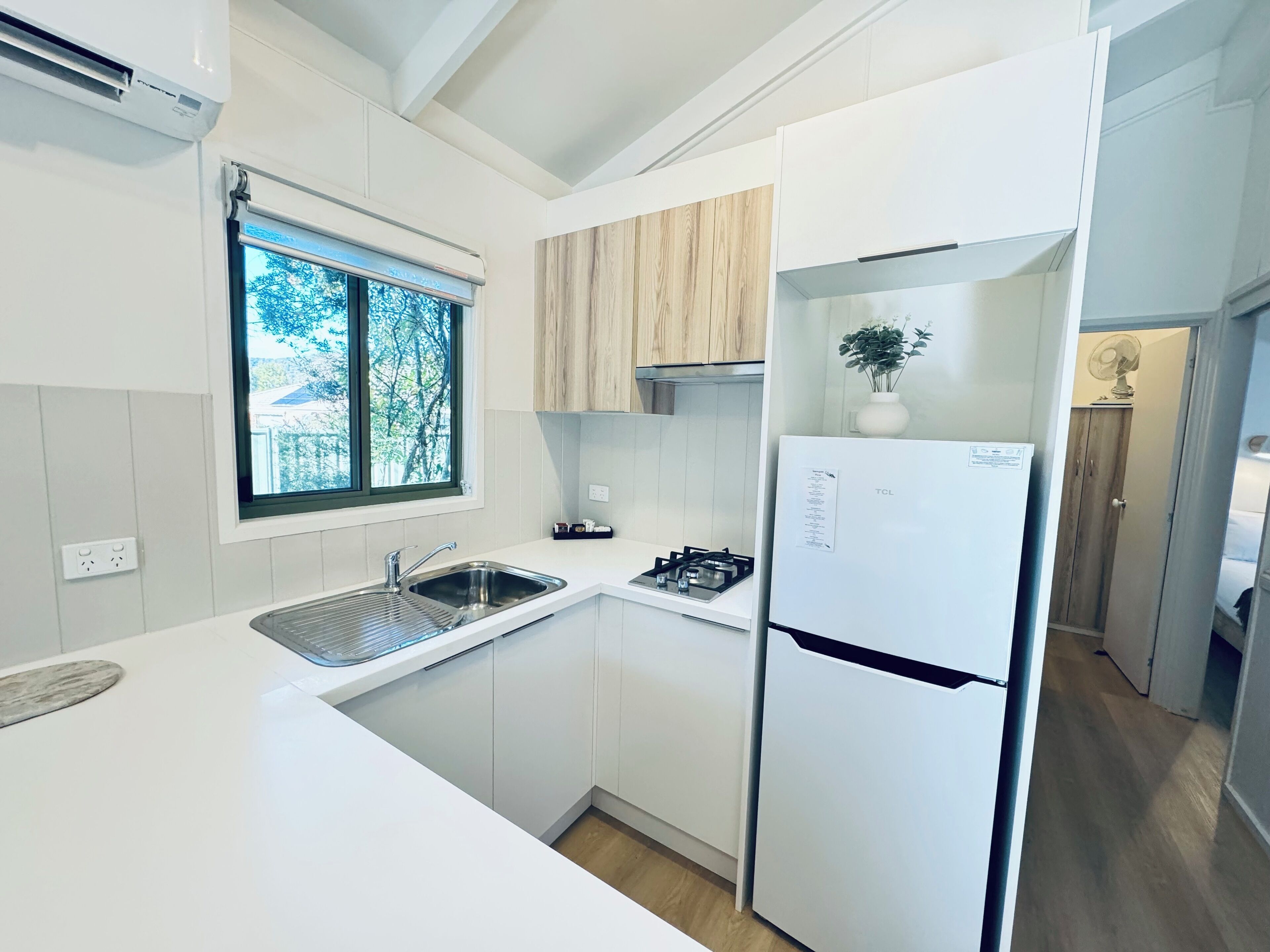 A compact kitchen with white cabinetry, a built-in gas stove, a stainless steel sink, and a white refrigerator.