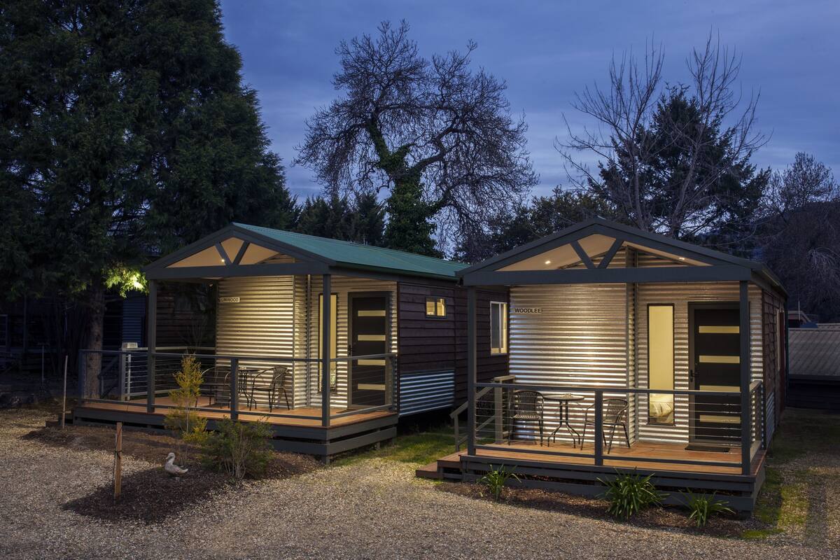 Two cabins with a deck and outdoor seating, surrounded by trees.