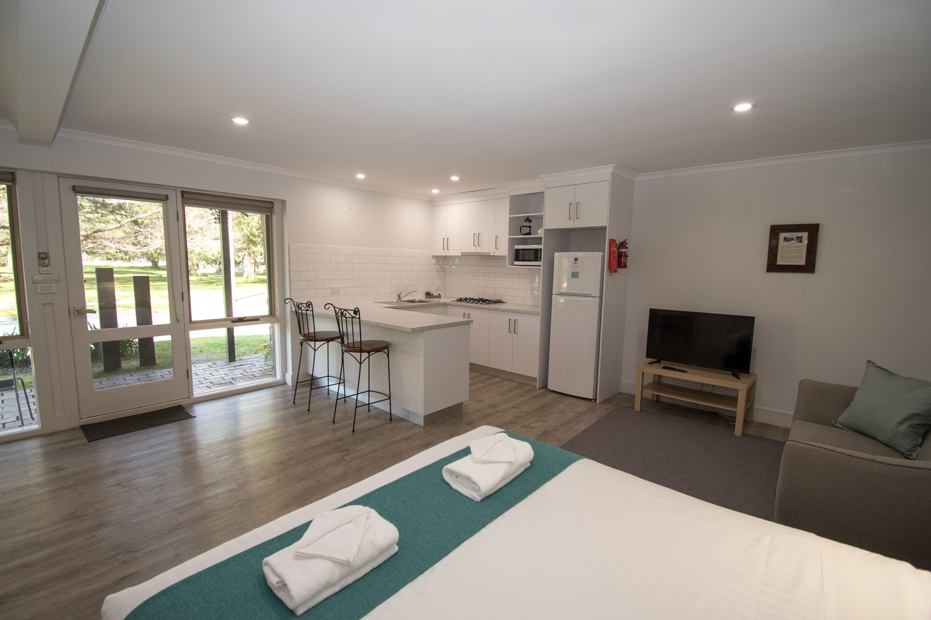 Habitación de hotel moderna con una cama grande, televisión, sofá, kitchenette y comedor con taburete de bar.