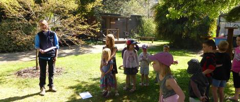 A group of children outdoors, possibly in a park or garden, with a wooden structure in the background.