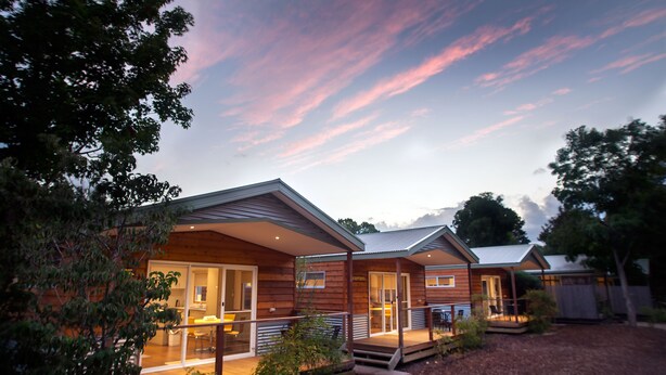 A modern log cabin with a porch and a small deck, surrounded by trees and a wooden fence. - Big4 Tasman Holiday Parks - Bright (Bright)