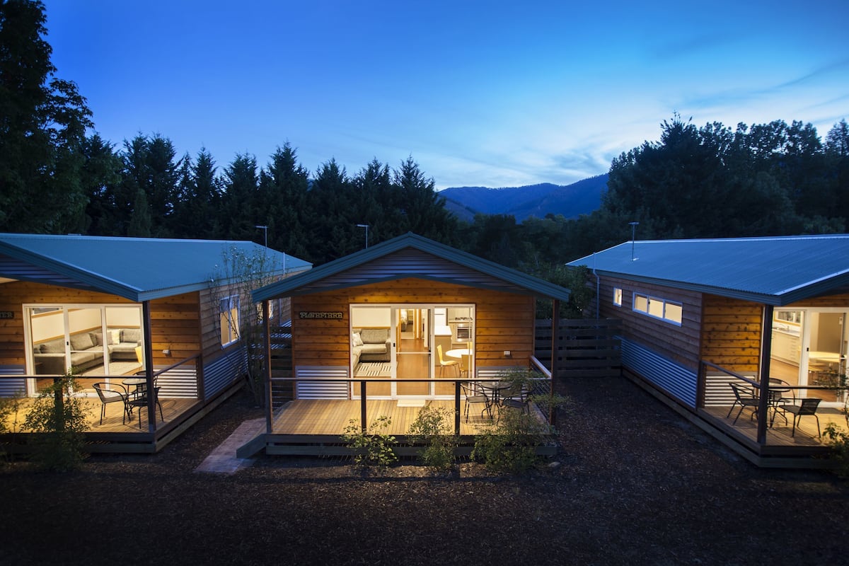 A modern cabin-style hotel with a central open-plan living area, a separate bedroom, and a dining area.