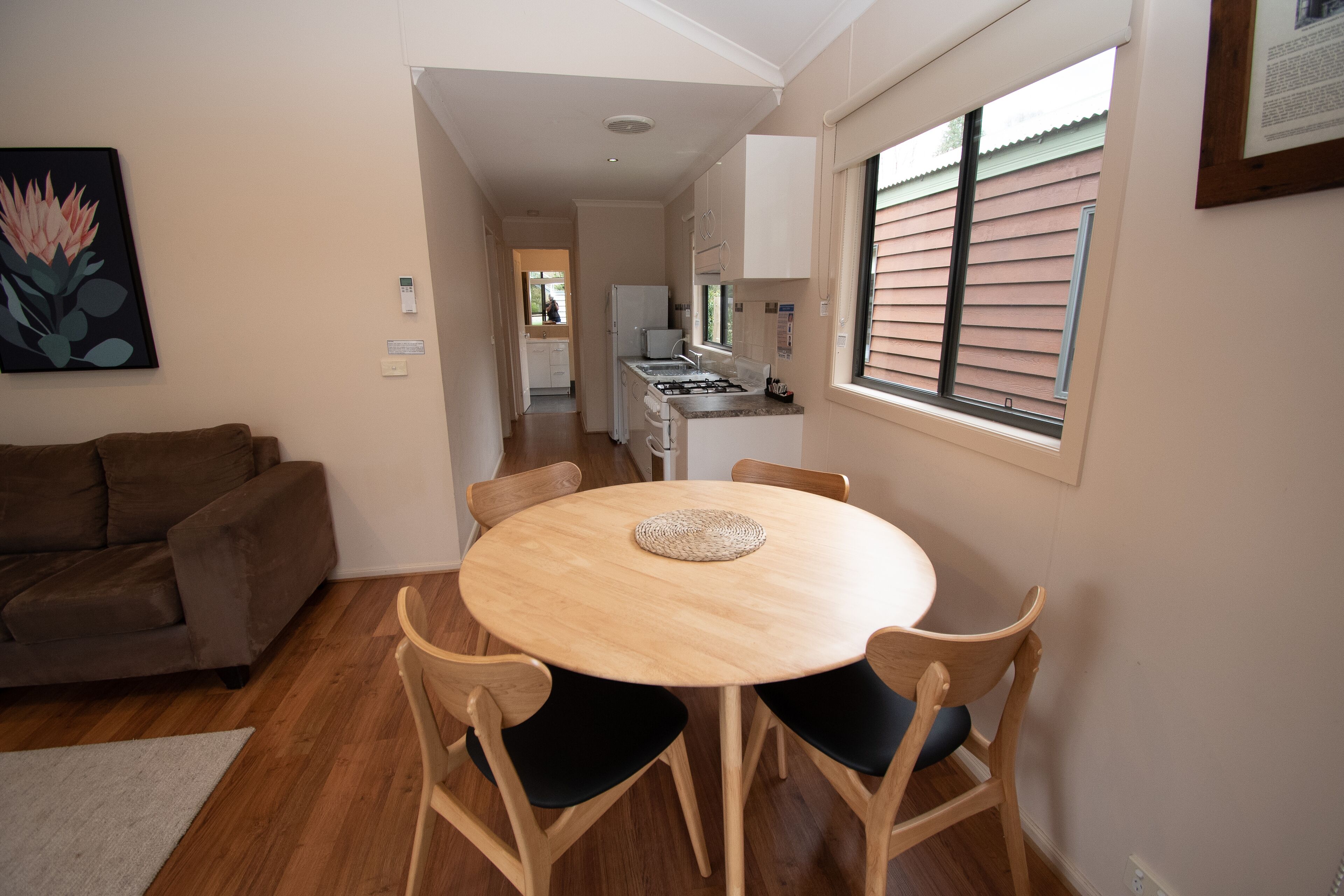 A dining area with a round table and chairs, a sofa, and a kitchen in the background.