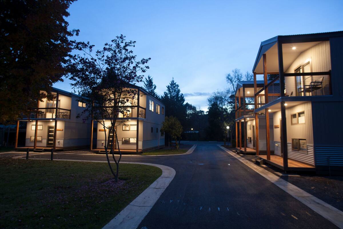 A modern residential area with two-story houses featuring large windows and balconies, surrounded by trees and a quiet street.