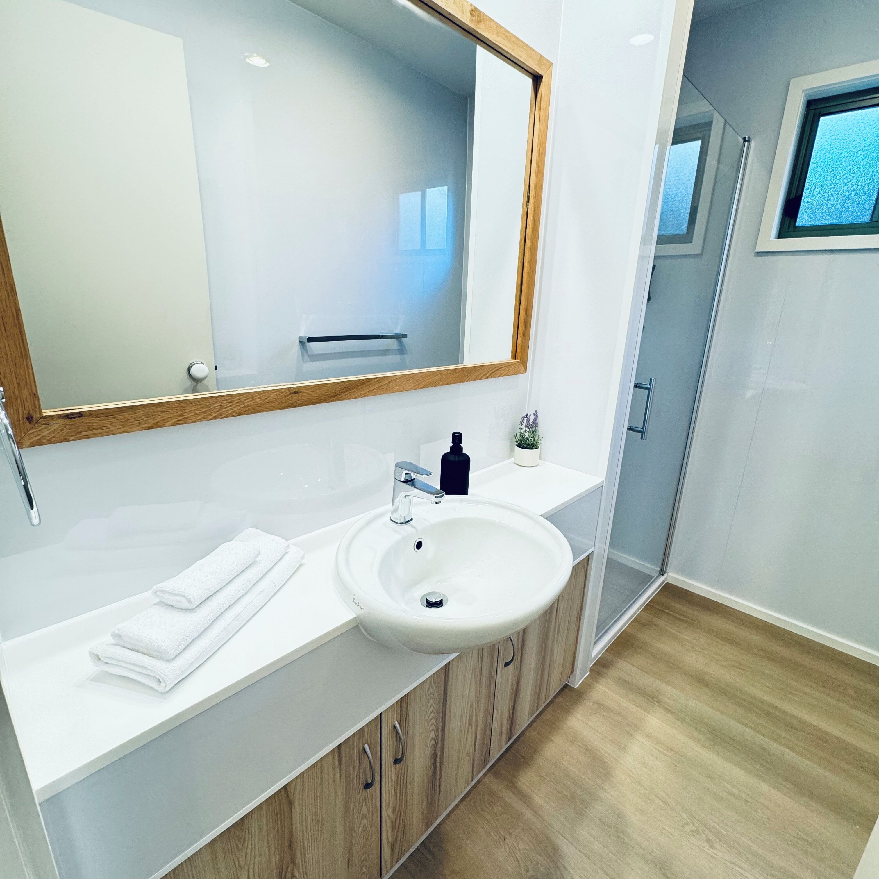 A modern bathroom with a large mirror, white sink, and wooden cabinets.