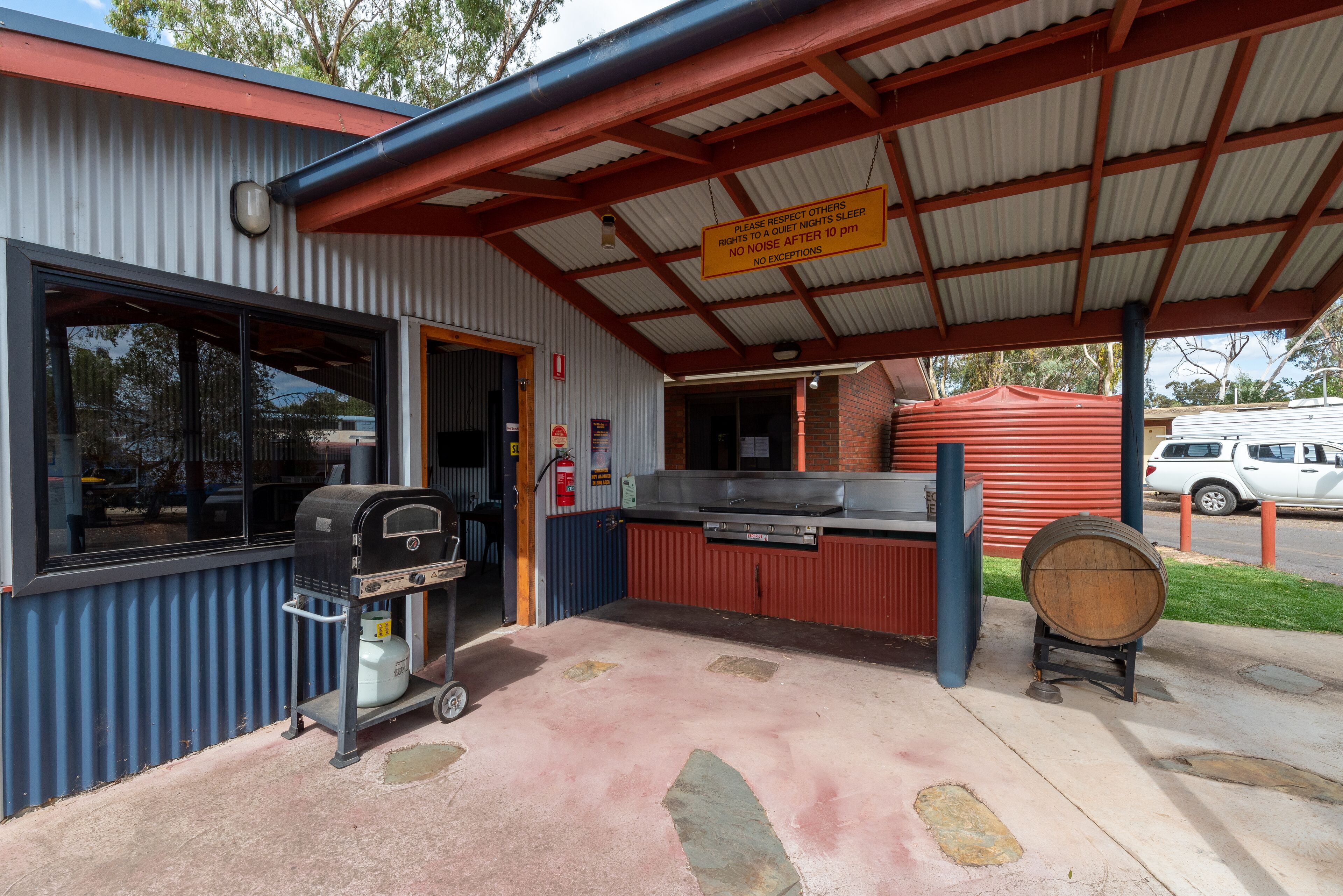 A covered outdoor area with a grill, a barrel, and a sign about quiet hours.
