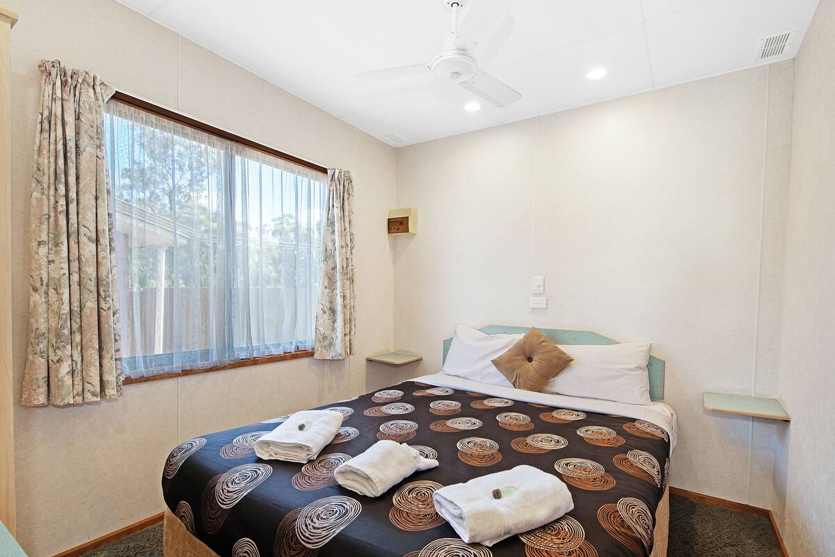 A hotel room with a bed, a nightstand, a window with curtains, and a ceiling fan.