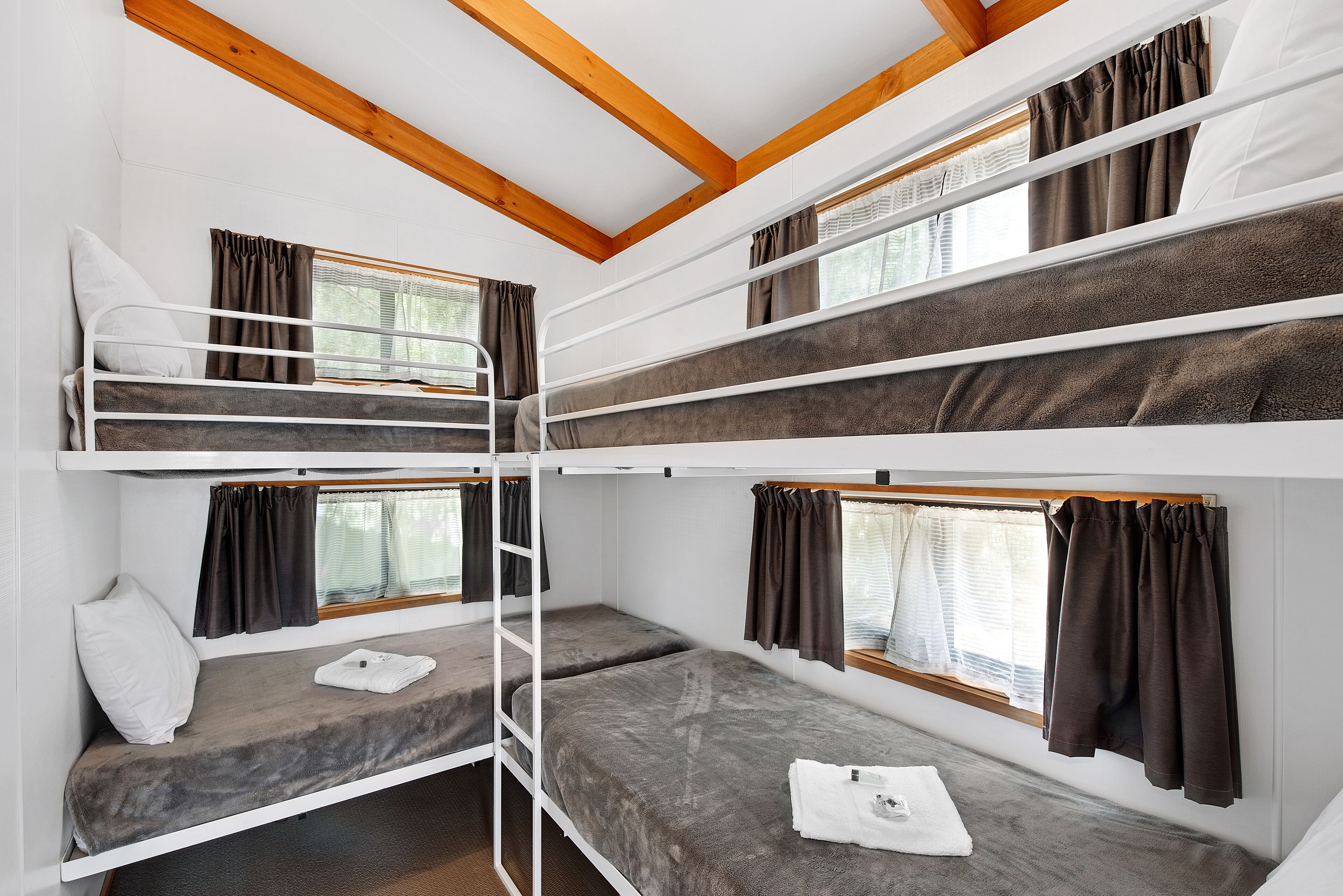 A bunk bed room with wooden beams, white walls, and curtains.