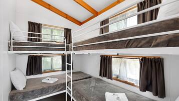 A bunk bed room with wooden beams, white walls, and curtains.