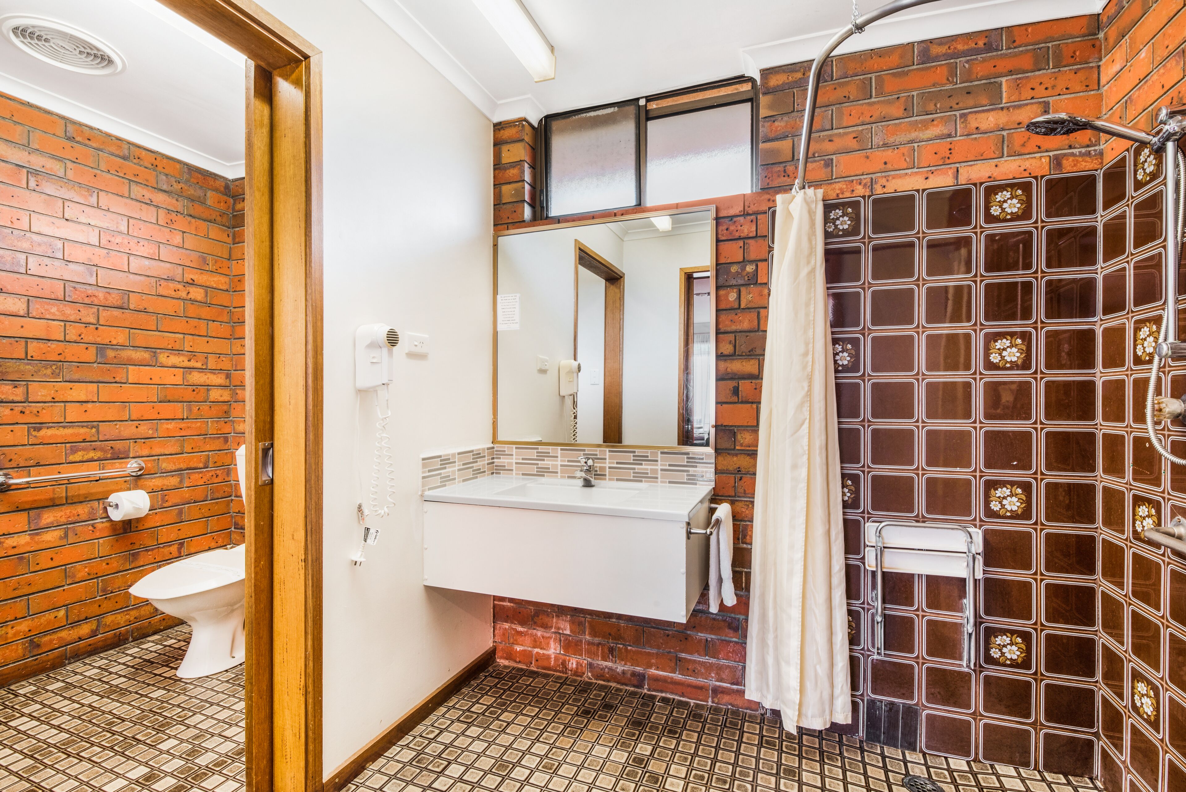 Un baño con lavamanos blanco, un espejo, ducha y retrete.